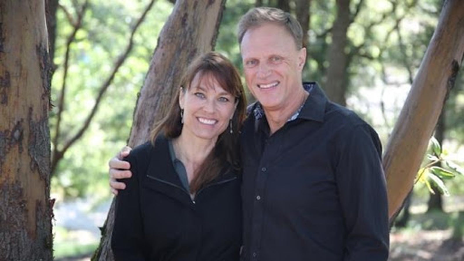 Greg and Patty de Vries, hosts of Living Well Event Center, smiling among madrone trees on their Los Gatos estate