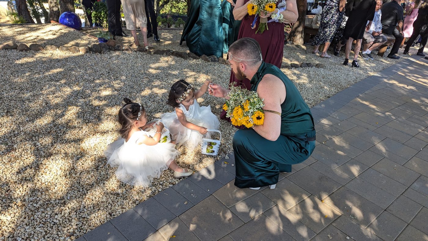 A groom sharing a moment with two flower girls before the ceremony at Living Well Event Center